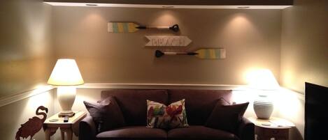 Relax in this inviting living room with a sofa, wall-mounted lamps, and a TV on a wooden stand.