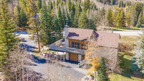 A single-story house with a chimney, surrounded by a forested area and a driveway leading to a parking area. - Nice Home in Great Vail Location! Hot Tub, Free Shuttle Access!! (Vail)