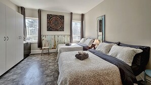A hotel room with two beds, a large window, a radiator, and a wardrobe. - Maison Zacharie (Desbiens)