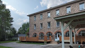 A stone building with multiple windows, a covered outdoor area, and a gravel path leading to the entrance. - Maison Zacharie (Desbiens)