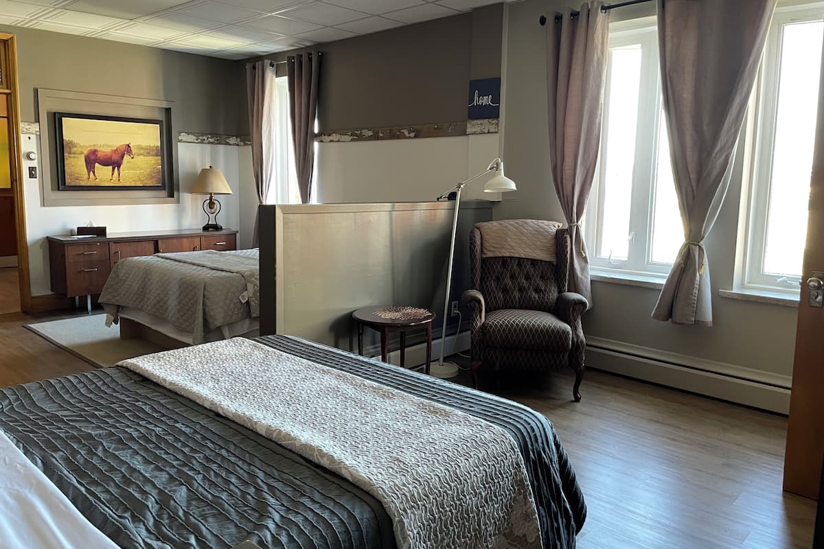 Ein Hotelzimmer mit einem großen Bett, einem Sessel, einem Schreibtisch und einem Fenster mit Vorhängen.