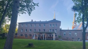 A large stone building with a prominent steeple and a covered entrance area. - Maison Zacharie (Desbiens)