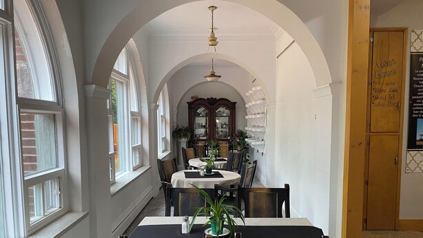 A dining area with a high arched ceiling, white walls, and a wooden door with a menu. - Maison Zacharie (Desbiens)