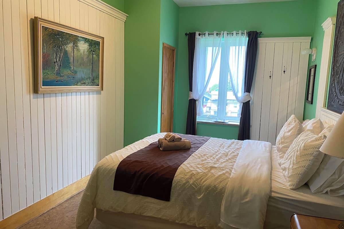 Ein Schlafzimmer mit einem Bett, einem Bild an der Wand, einem Fenster mit Vorhängen und einer Tür.