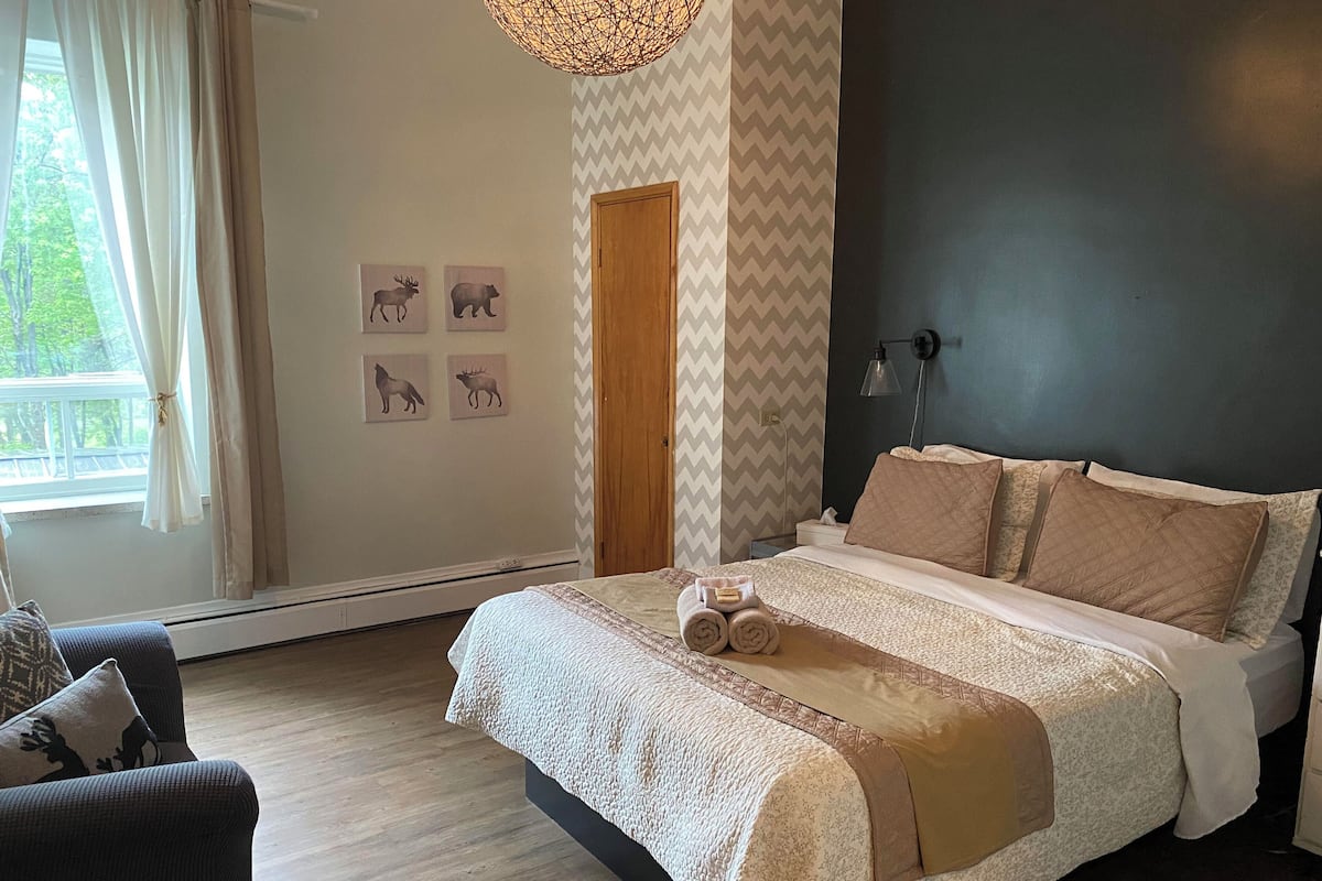 Ein Schlafzimmer mit Bett, Stuhl, einem Fenster mit Vorhängen und Wandbildern.