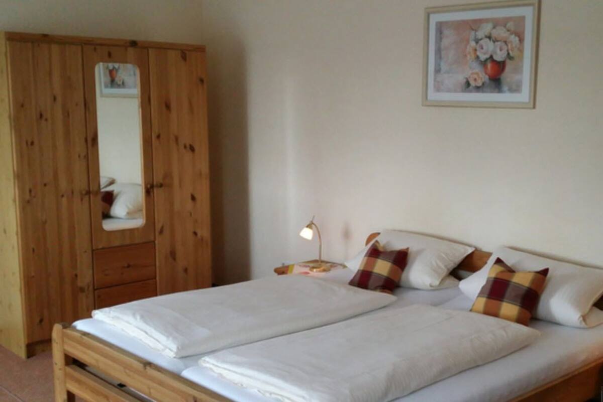 Een slaapkamer met een houten garderobe, een bed met witte lakens en een bedlampje.