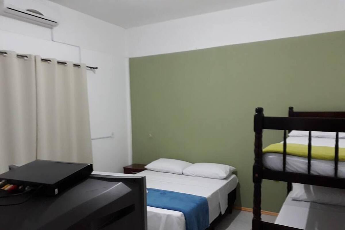 Une chambre avec un lit superposé, un bureau avec un ordinateur, une table de chevet et un lit recouvert d’une couverture bleue et blanche.