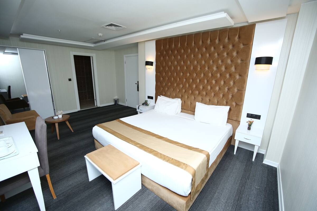 Una habitación de hotel con una cama grande, una mesita de noche, una silla, un escritorio y una pequeña mesa con lámpara.