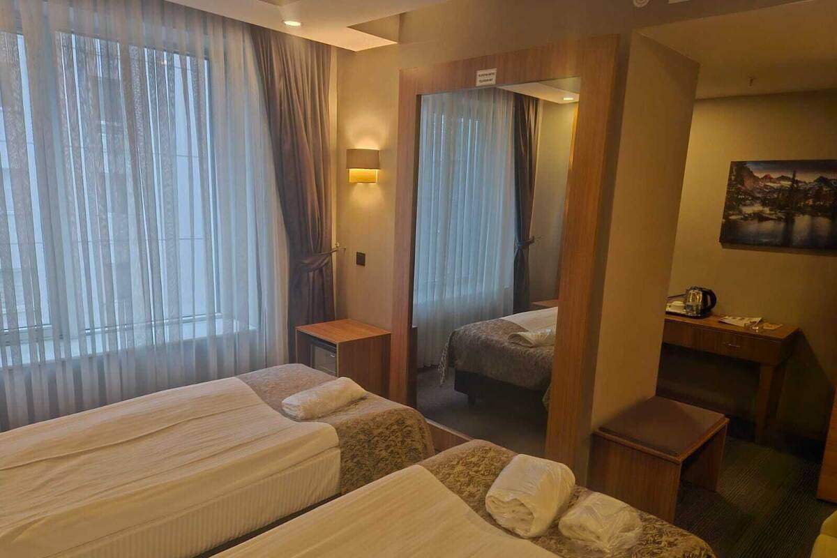 Habitación de hotel con dos camas, un escritorio, una silla, un espejo y un cuadro en la pared.