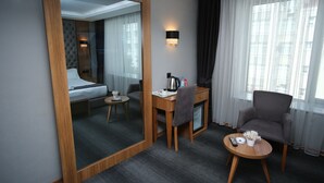 Camera d'albergo con un letto, una scrivania con una sedia, un tavolino con un telecomando, una macchina del caffè e una pianta decorativa.
