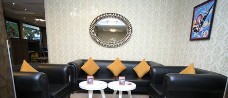 Um hall com um sofá de couro preto, duas mesinhas brancas e um espelho decorativo na parede.