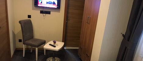 A hotel room with a bed, a small table with a remote control, a chair, and a television mounted on the wall.