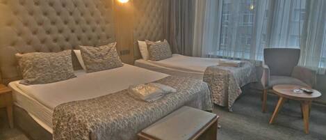A hotel room with two beds, a small table, a chair, and a large window with curtains.