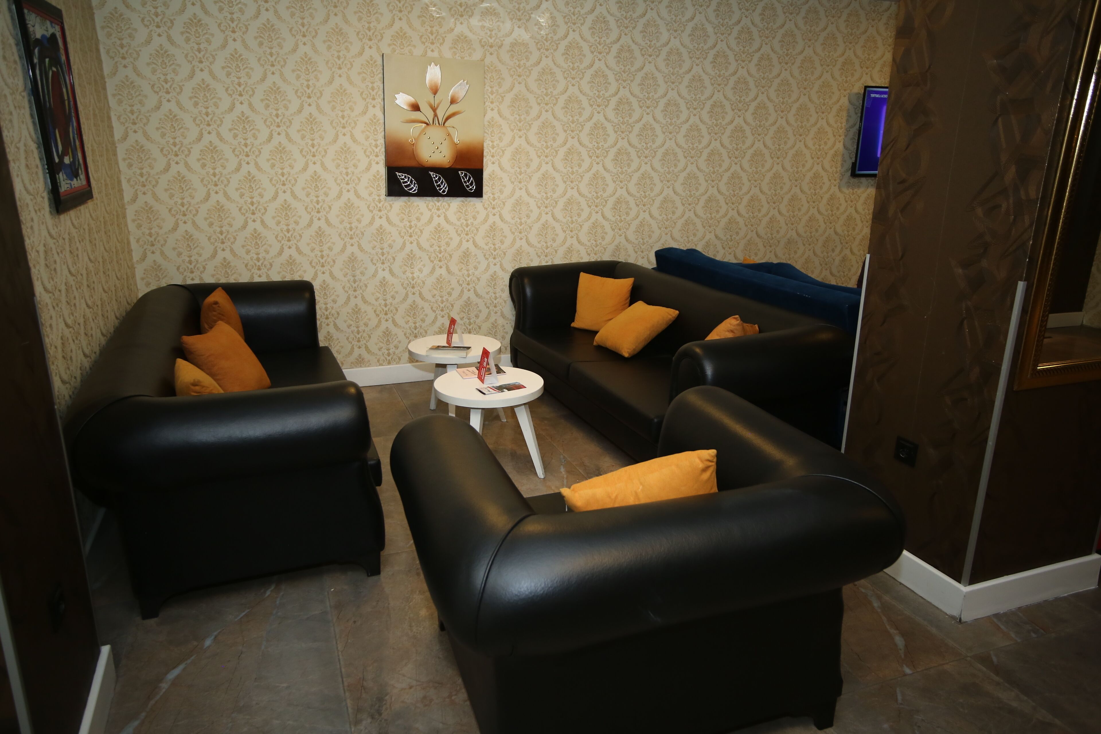 A living room with two black leather sofas, a small white table, and patterned wallpaper.