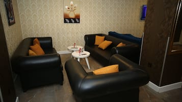 A living room with two black leather sofas, a small white table, and patterned wallpaper.