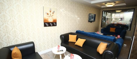 A modern lounge area with a black leather sofa, white coffee tables, and patterned wallpaper.