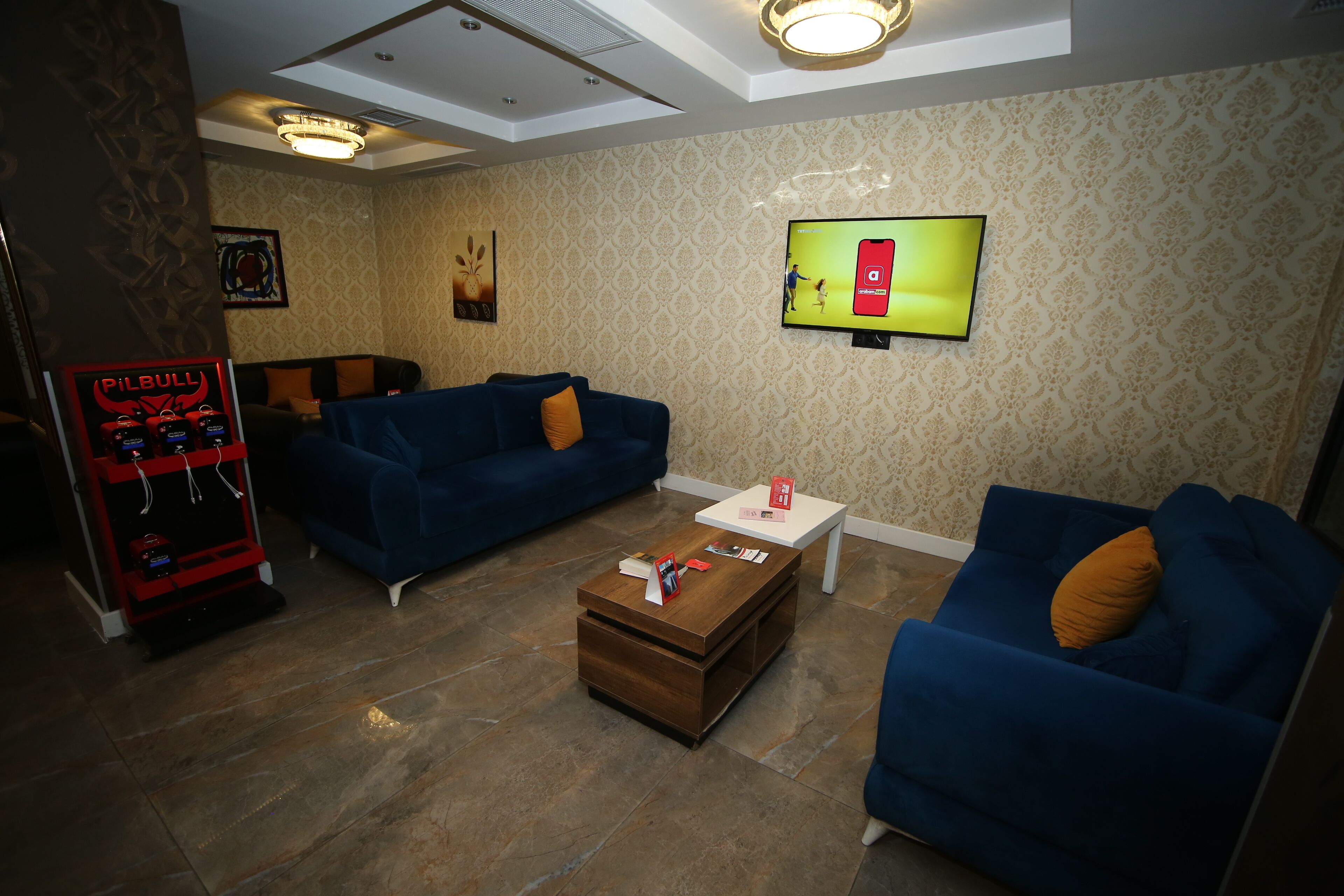 A living room with two blue sofas, a coffee table, a TV mounted on the wall, and a red arcade machine.