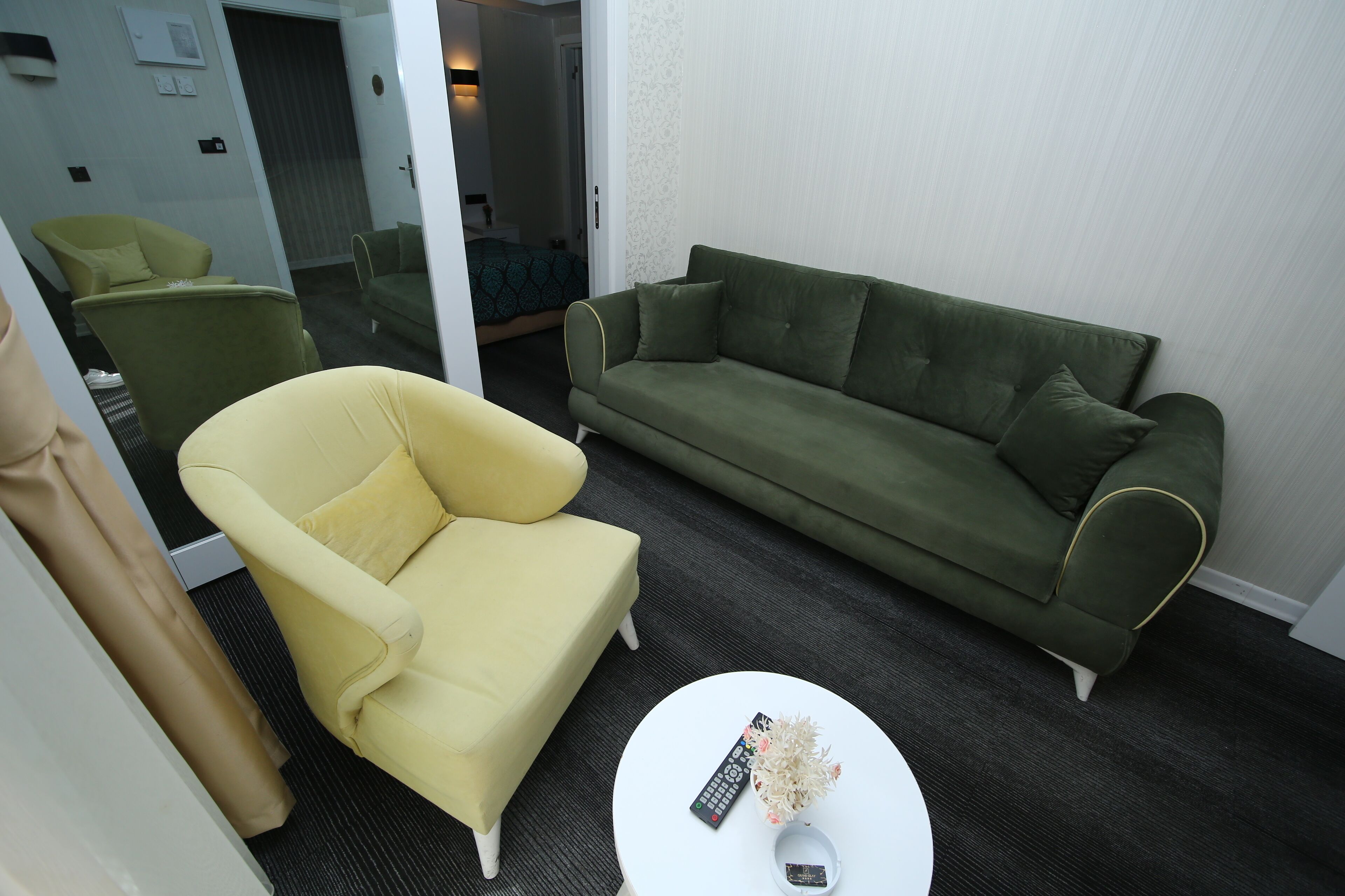 A living room with a yellow armchair, a green sofa, and a white coffee table with a remote control and decorative item.