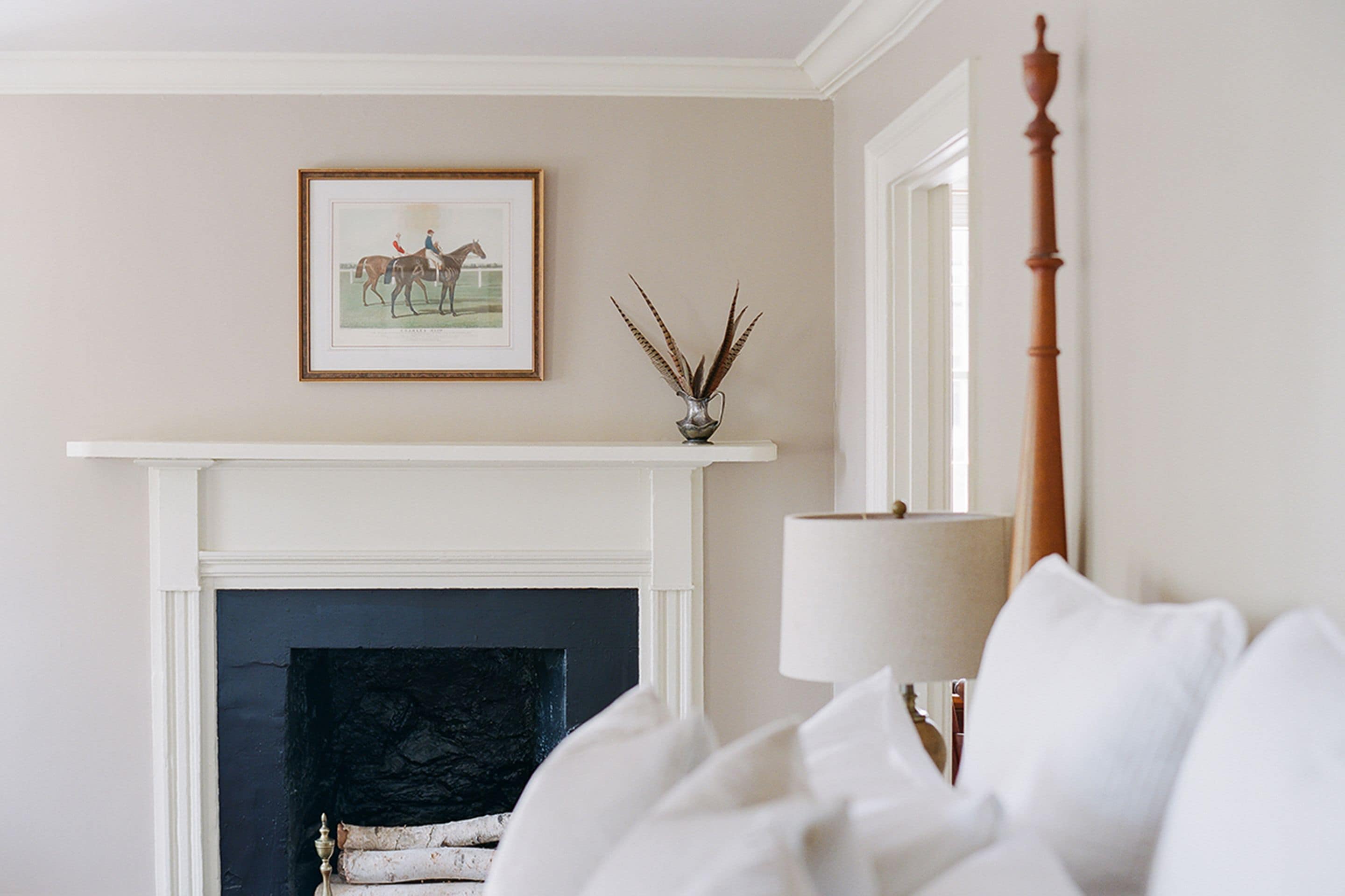 A bedroom with a fireplace, a framed picture above it, and a bedside lamp.