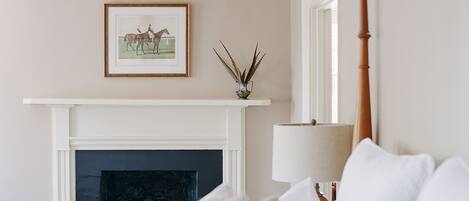 A bedroom with a fireplace, a framed picture above it, and a bedside lamp.