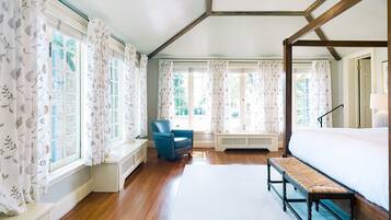 A bedroom with a four-poster bed, a bench, a chair, and large windows with curtains.