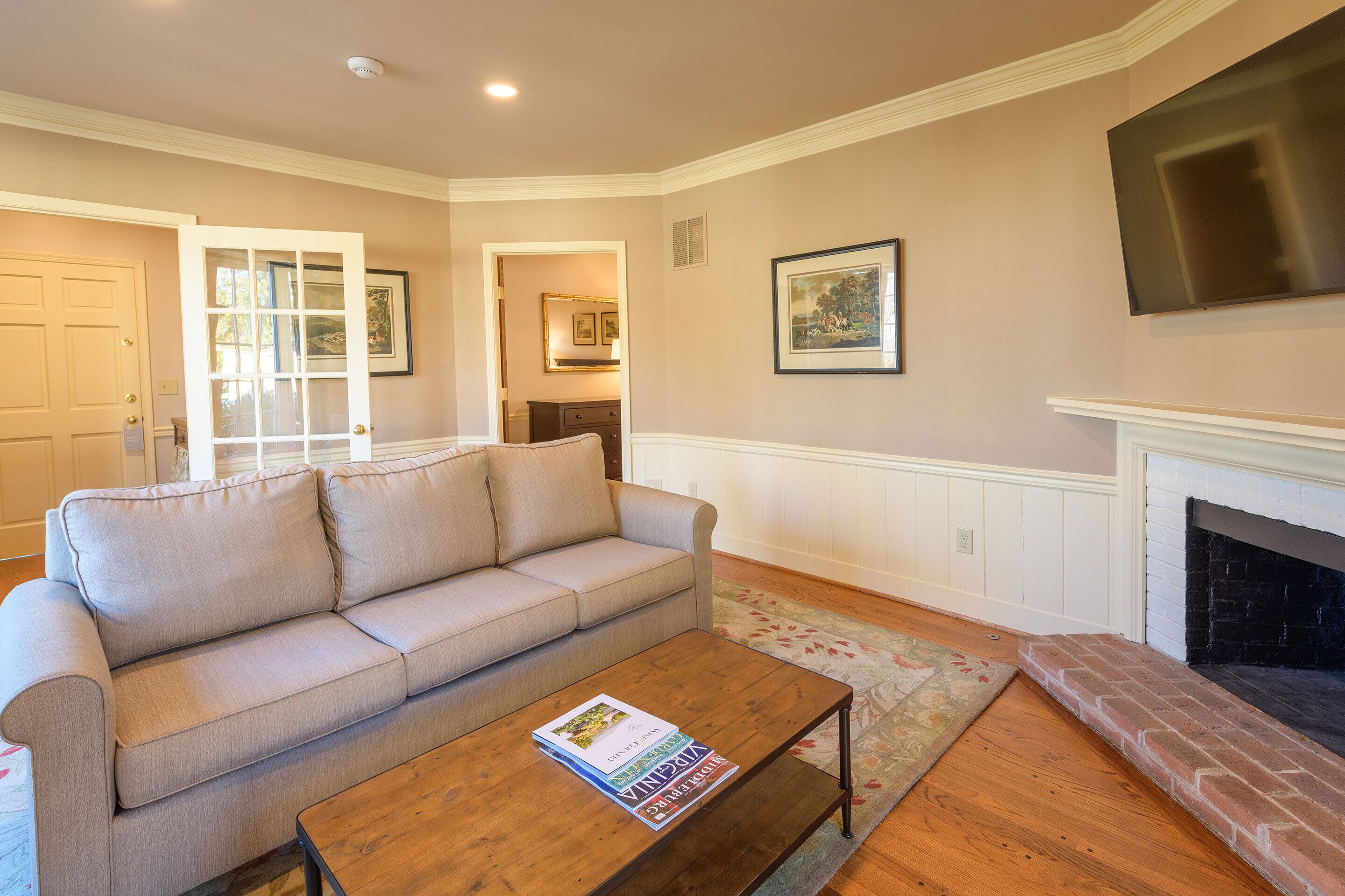 A living room with a beige sofa, a wooden coffee table, a fireplace, and a flat-screen TV mounted on the wall.