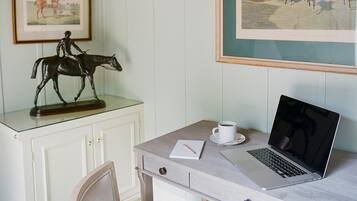 Une pièce comprenant un bureau, un ordinateur portable, une tasse, un tableau représentant un cheval et une chaise.