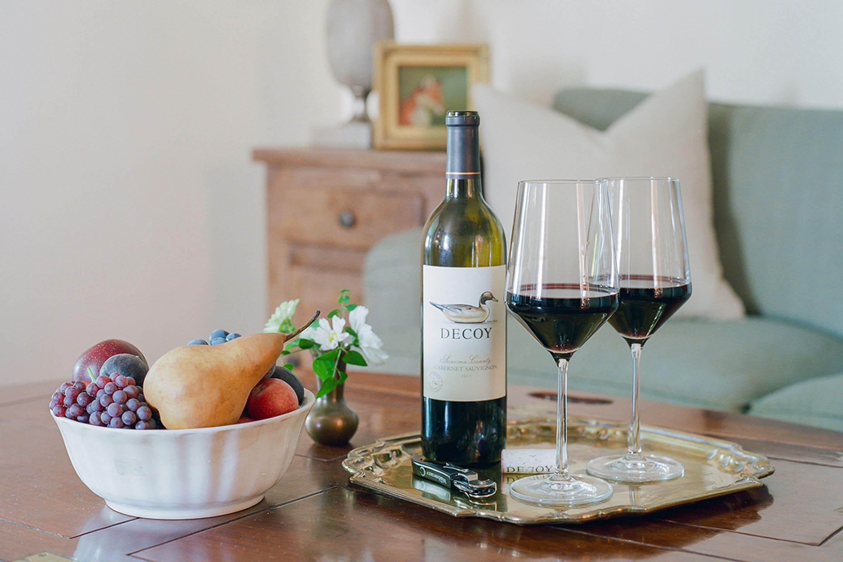 A bottle of wine, two wine glasses, and a bowl of fruit on a tray.