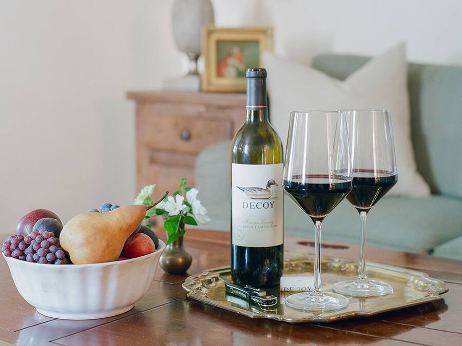 A bottle of wine, two wine glasses, and a bowl of fruit on a tray.