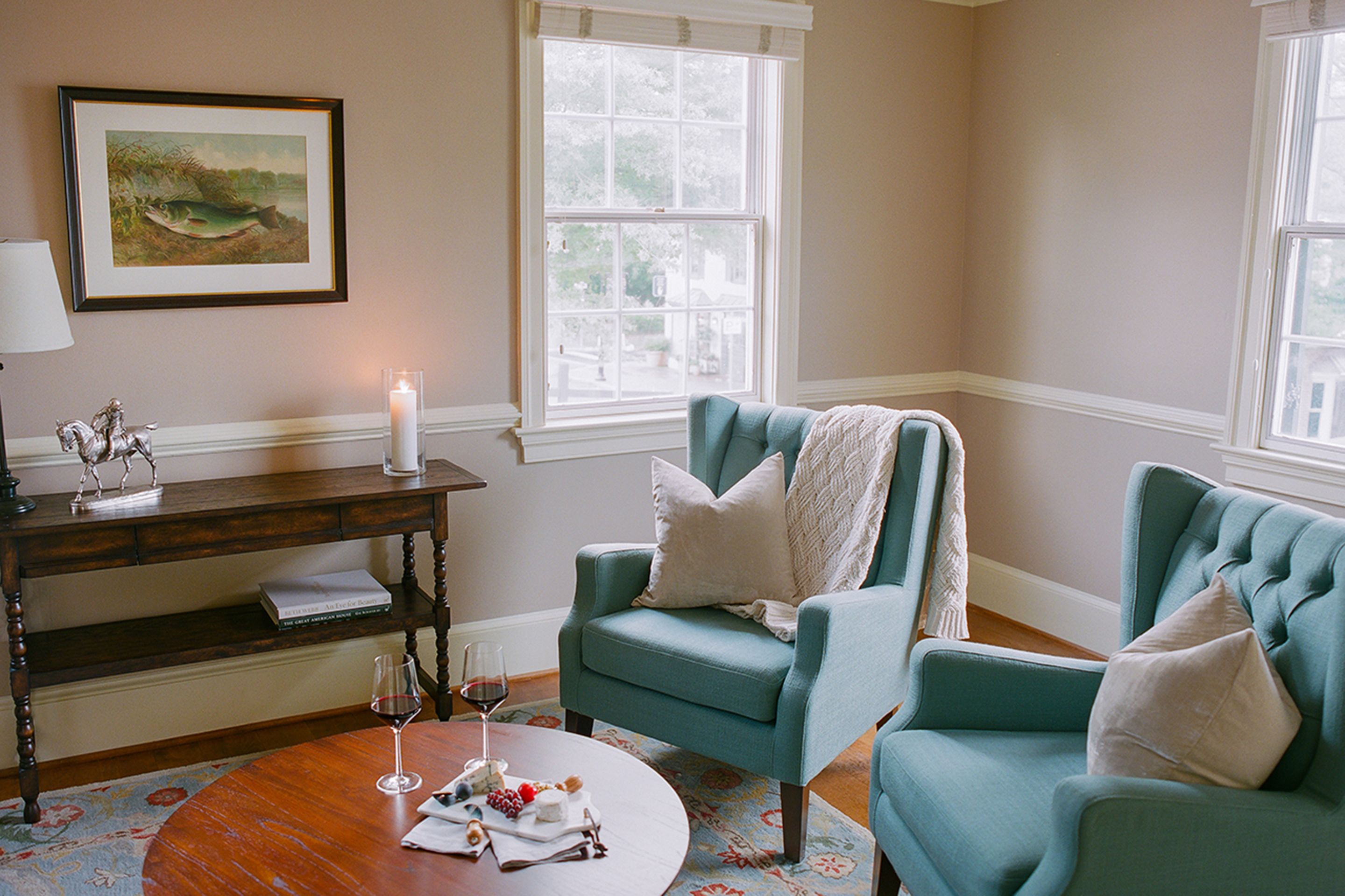 A cozy room with a teal armchair, a wooden table with a candle, and a framed painting on the wall.