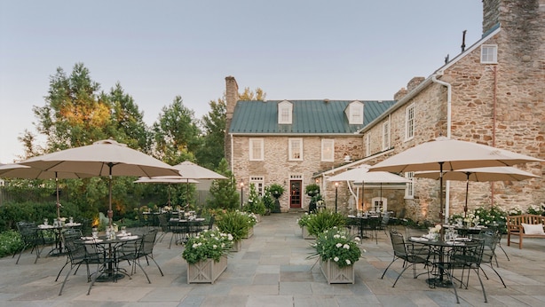 An outdoor patio area with stone tables and chairs, surrounded by potted plants and umbrellas.
