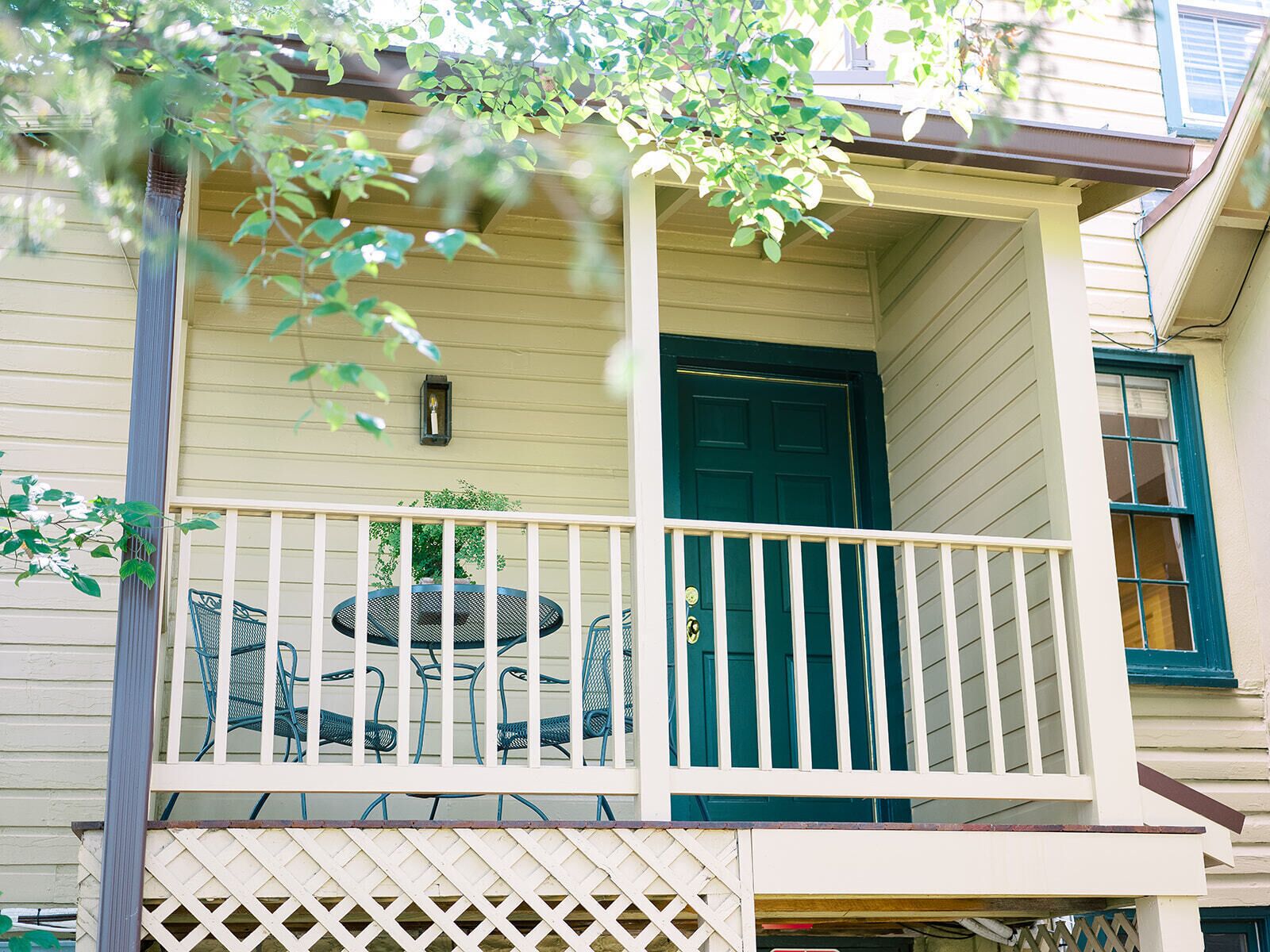 A two-story house with a covered porch, a green door, and a small table with chairs.