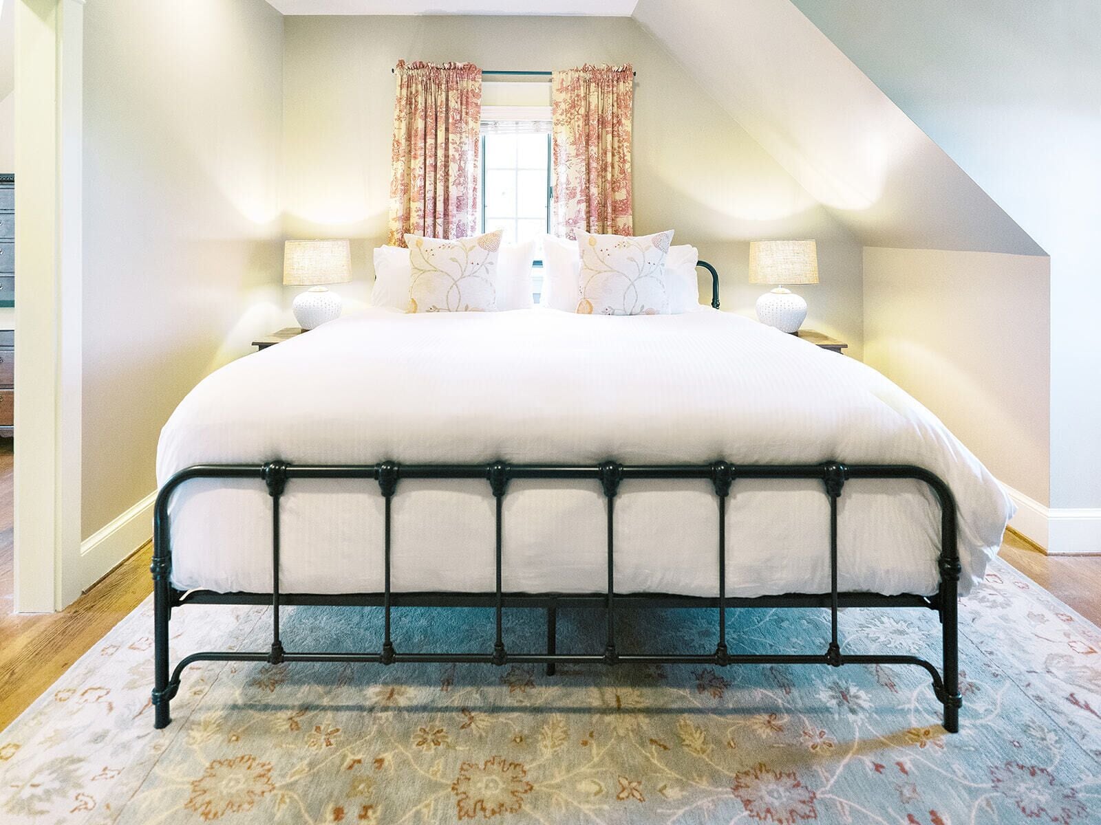 Une chambre à coucher avec un grand lit, deux tables de chevet et une fenêtre avec des rideaux.