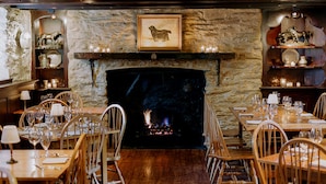 A dining area with a fireplace, wooden chairs, and tables set for a meal.
