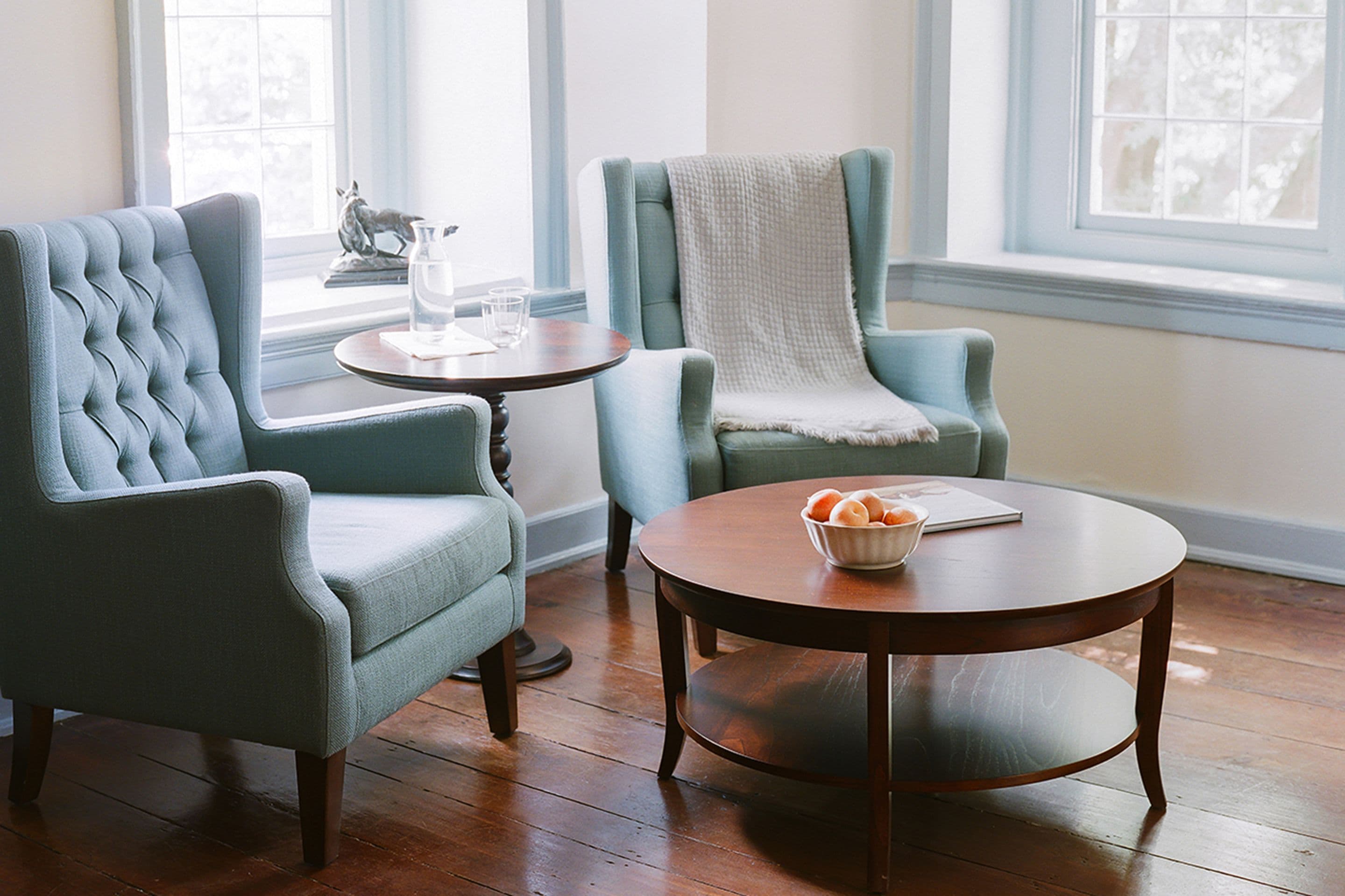 Una habitación con dos sillones tapizados, una mesa de centro de madera y una mesita auxiliar.