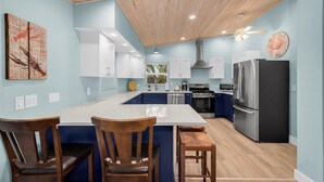 A modern kitchen with a central island, white cabinets, and a stainless steel refrigerator. - AMI North End Private Heated Pool.  1.2 Block to Gulf Beach! (Anna Maria)