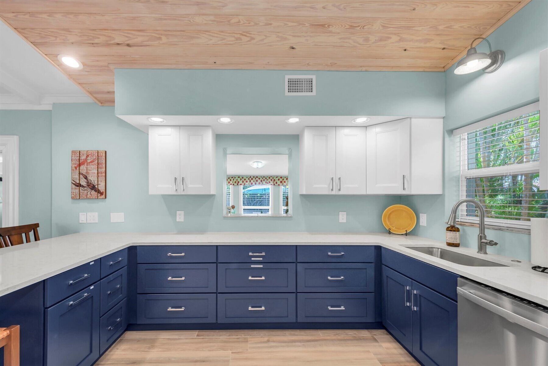 A modern kitchen with white upper cabinets, dark blue lower cabinets, a white countertop, and a stainless steel sink.