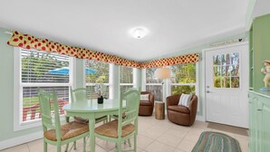 A room with a dining table and chairs, a sofa, a lamp, and a door with a view of palm trees. - AMI North End Private Heated Pool.  1.2 Block to Gulf Beach! (Anna Maria)