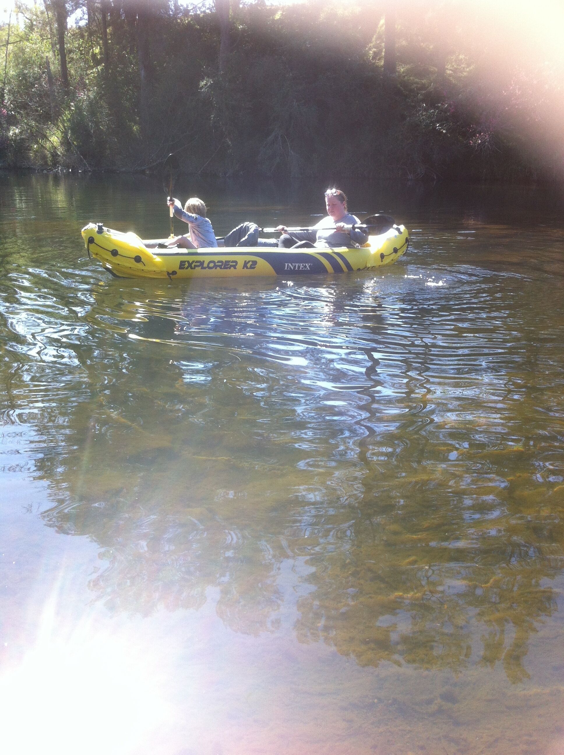 A yellow inflatable boat with two people on it, floating on water.
