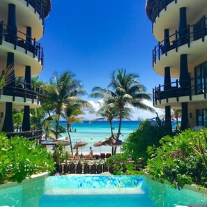 A resort pool with a view of the ocean and palm trees.