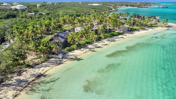 An aerial view of a beach resort with multiple bungalow-style accommodations, clear turquoise waters, and lush greenery.