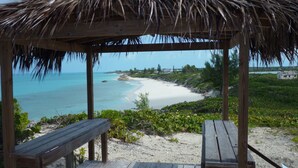 A wooden gazebo with a thatched roof overlooking a beach.