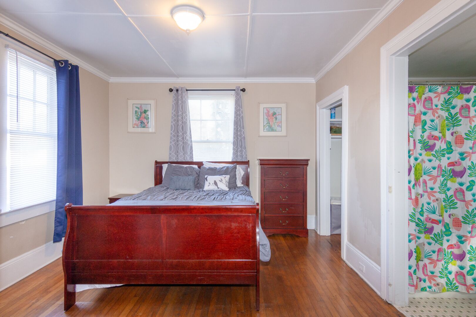 A bedroom with a wooden bed, a dresser, and a window with curtains.