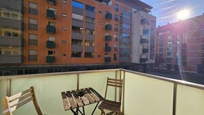 A balcony with a wooden table and chairs, overlooking a multi-story building with balconies. - Anita Tour As / Central 1BR App, free garage, AC, Wi-Fi, 7min walk from old town (Ljubljana)