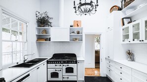A compact kitchen with white cabinetry, a black stove, and a chandelier. - Corvah House, Beautiful Corvah House circa 1860, restored and beaming with grandeur and comfort (Castlemaine)