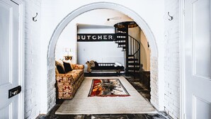 A hallway with a white brick wall, a patterned sofa, a rug, and a staircase leading to a room labeled "BUTCHER". - Corvah House, Beautiful Corvah House circa 1860, restored and beaming with grandeur and comfort (Castlemaine)