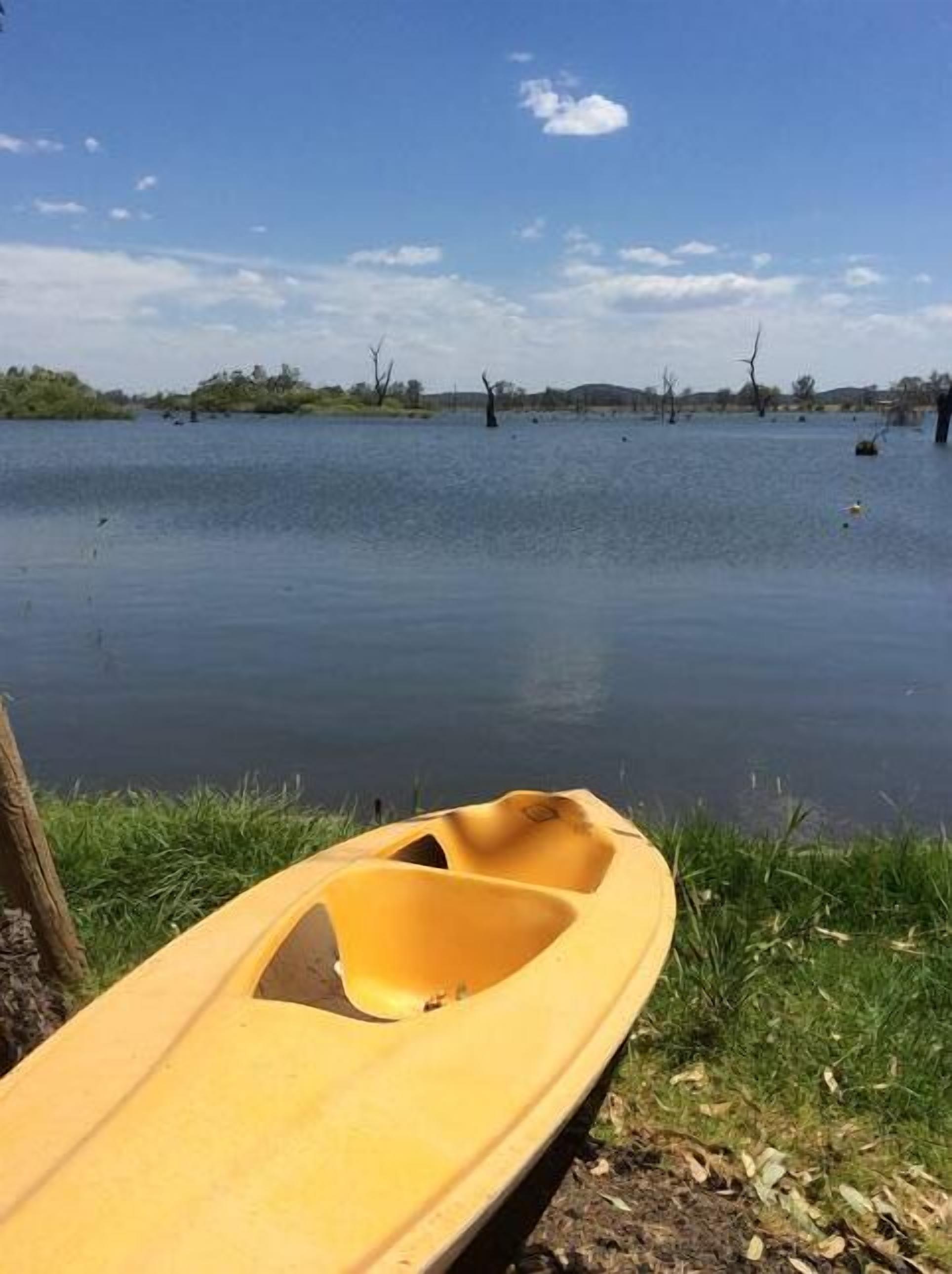 Un kayak giallo sulla riva di un lago calmo, con sponde erbose e alberi sullo sfondo.