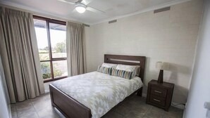 A bedroom with a bed, curtains, a nightstand, and a ceiling fan. - Foxy Lodge - Lakeside getaway (Nagambie)