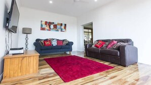 A modern living room with a wooden floor, two sofas, a red rug, a ceiling fan, and a flat-screen TV. - Foxy Lodge - Lakeside getaway (Nagambie)