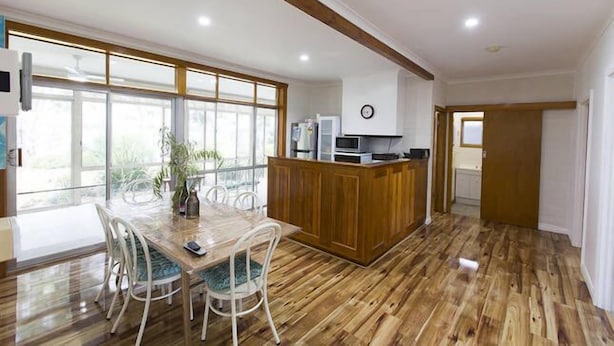 A spacious kitchen with a wooden island, large windows, and a dining area with white chairs. - Foxy Lodge - Lakeside getaway (Nagambie)